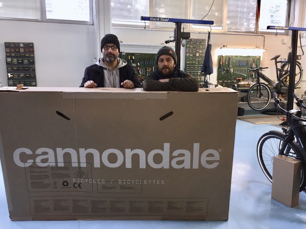 Due meccanici davanti a una scatola contenente una nuova bicicletta Cannondale